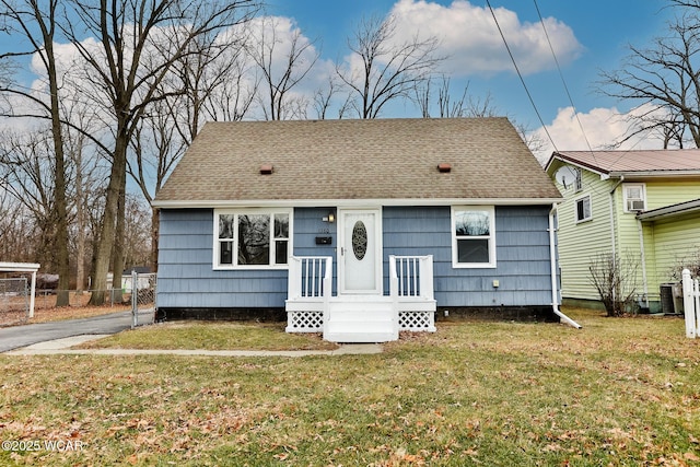 bungalow-style home featuring a shingled roof, fence, and a front lawn