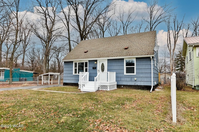 bungalow-style house with a shingled roof, fence, and a front lawn