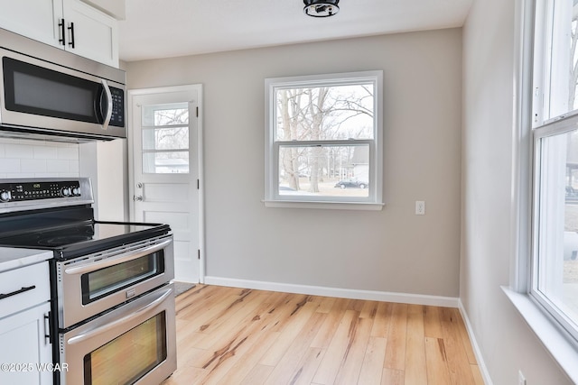 kitchen with baseboards, stainless steel appliances, light countertops, light wood-style floors, and white cabinetry