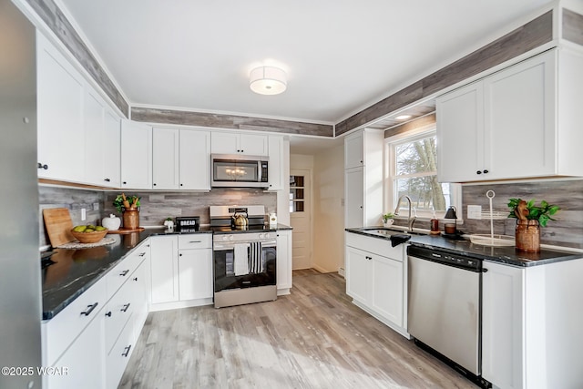 kitchen with appliances with stainless steel finishes, sink, backsplash, white cabinets, and light hardwood / wood-style floors