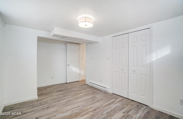 unfurnished bedroom with a closet, light hardwood / wood-style flooring, and baseboard heating