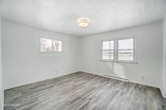 unfurnished room with a baseboard heating unit and light wood-type flooring