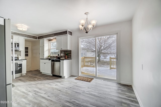 kitchen featuring appliances with stainless steel finishes, a chandelier, white cabinetry, decorative light fixtures, and light hardwood / wood-style flooring