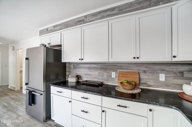 kitchen featuring light hardwood / wood-style flooring, stainless steel fridge, backsplash, white cabinets, and dark stone counters