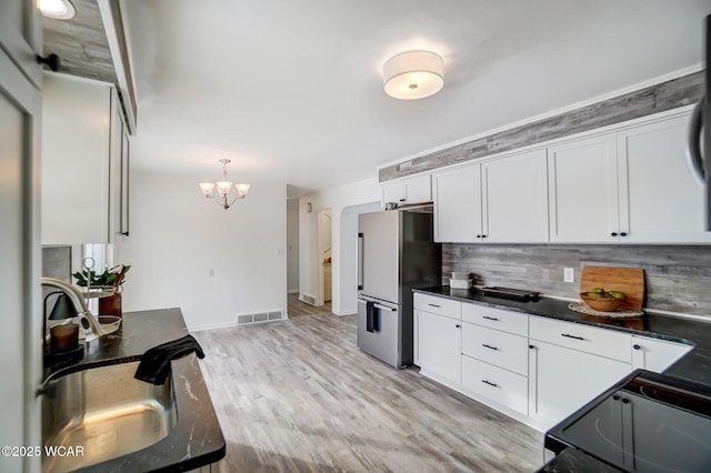 kitchen with pendant lighting, black electric range, tasteful backsplash, white cabinetry, and stainless steel refrigerator