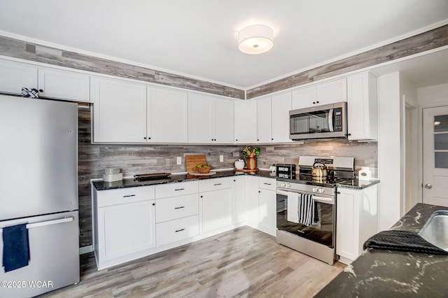 kitchen with white cabinets, appliances with stainless steel finishes, dark stone counters, backsplash, and light hardwood / wood-style flooring