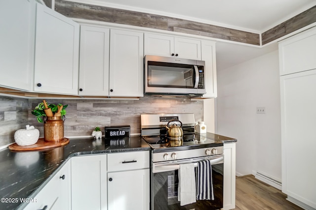 kitchen with baseboard heating, appliances with stainless steel finishes, wood-type flooring, white cabinetry, and tasteful backsplash