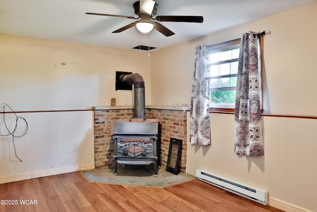 4940 Stewart Rd, Lima, OH 45801 - living area featuring a baseboard heating unit, a wood stove, wood finished floors, a ceiling fan, and wainscoting
