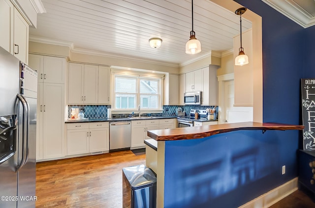 kitchen featuring hanging light fixtures, ornamental molding, kitchen peninsula, and appliances with stainless steel finishes