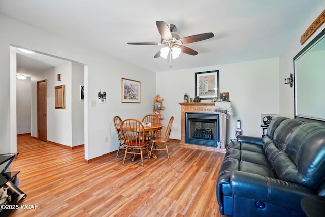 living area with baseboards, light wood-style flooring, a fireplace, and ceiling fan