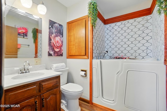 full bathroom with washer / clothes dryer, toilet, a bath, vanity, and wood finished floors