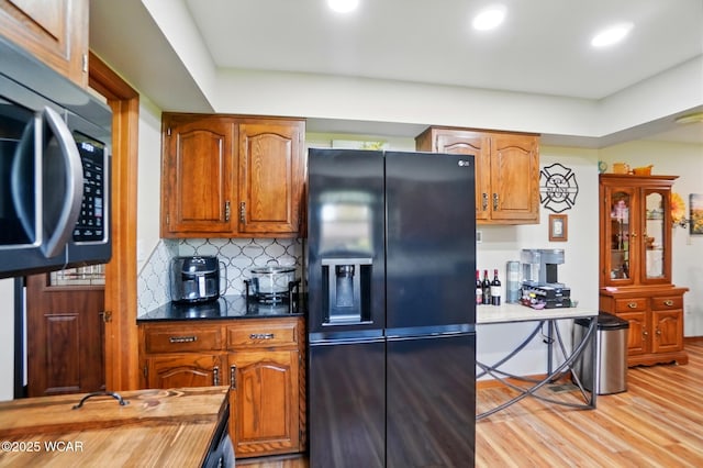 kitchen featuring stainless steel microwave, brown cabinetry, black refrigerator with ice dispenser, recessed lighting, and light wood-style flooring