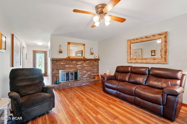 living room with a brick fireplace, a ceiling fan, and wood finished floors