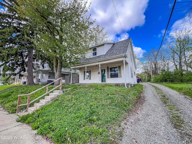 bungalow-style home with a porch, roof with shingles, and gravel driveway