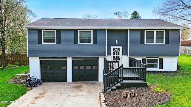 split foyer home with driveway, a shingled roof, an attached garage, fence, and a front lawn