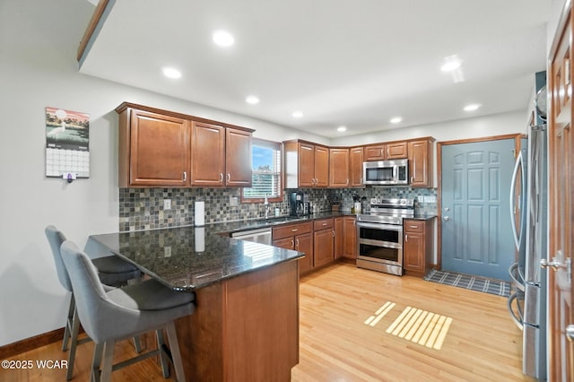 13286 Arrowhead Dr, Findlay, OH 45840 - kitchen featuring appliances with stainless steel finishes, a peninsula, decorative backsplash, light wood finished floors, and brown cabinetry
