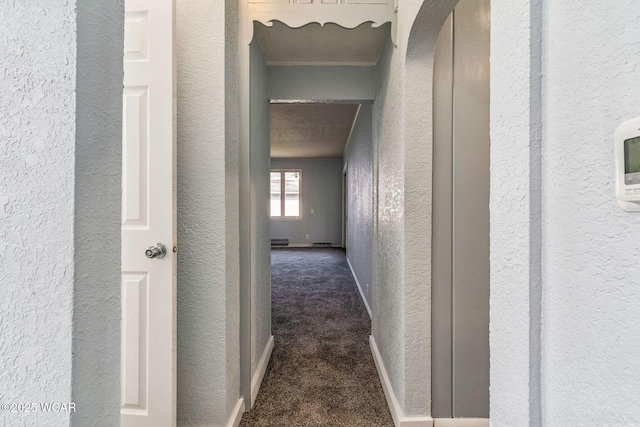 hallway with a textured wall, baseboards, and dark carpet