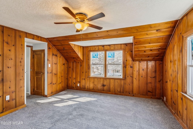 bonus room with ceiling fan, wooden walls, carpet floors, and a textured ceiling