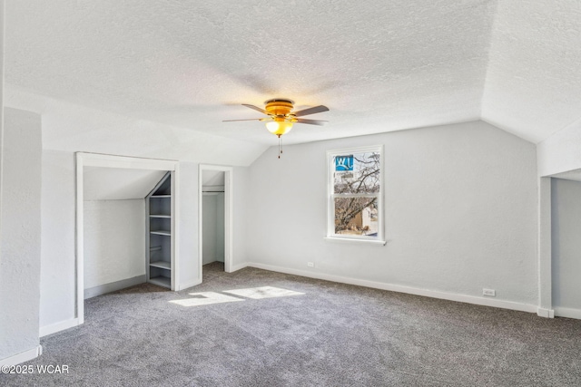 unfurnished bedroom featuring multiple closets, lofted ceiling, a textured ceiling, carpet, and baseboards