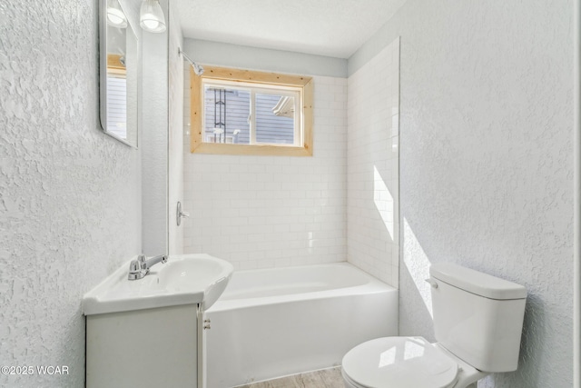 full bathroom featuring toilet, vanity, shower / bathing tub combination, and a textured wall