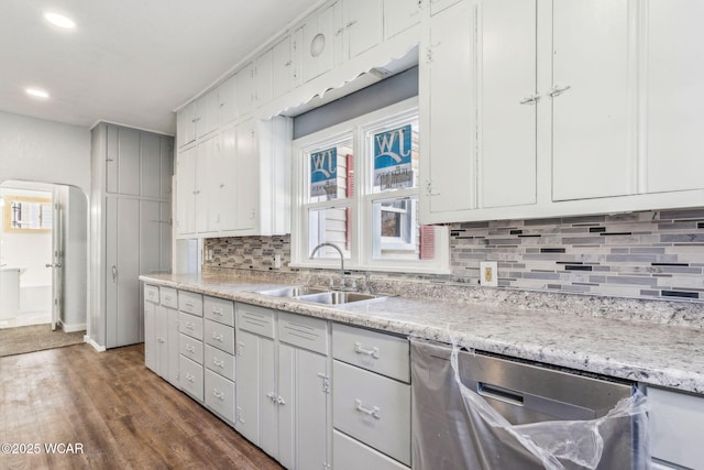 kitchen featuring a sink, backsplash, arched walkways, light countertops, and dishwasher