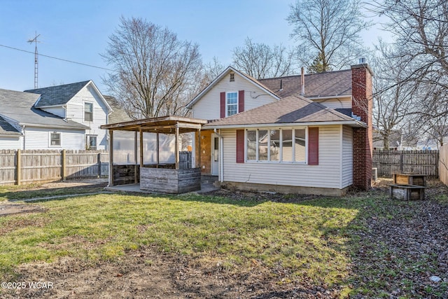 rear view of property featuring a lawn, a fenced backyard, a chimney, and a shingled roof