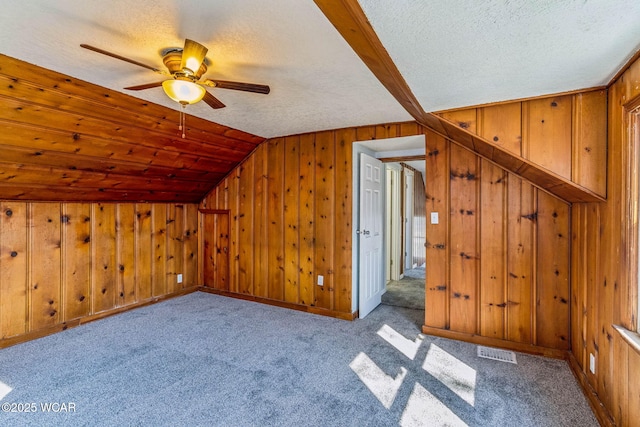 additional living space with lofted ceiling, wooden walls, visible vents, and a textured ceiling