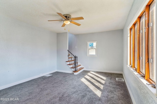 empty room with stairway, visible vents, baseboards, a textured ceiling, and dark carpet