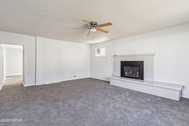 unfurnished living room featuring a brick fireplace, dark colored carpet, and a textured ceiling