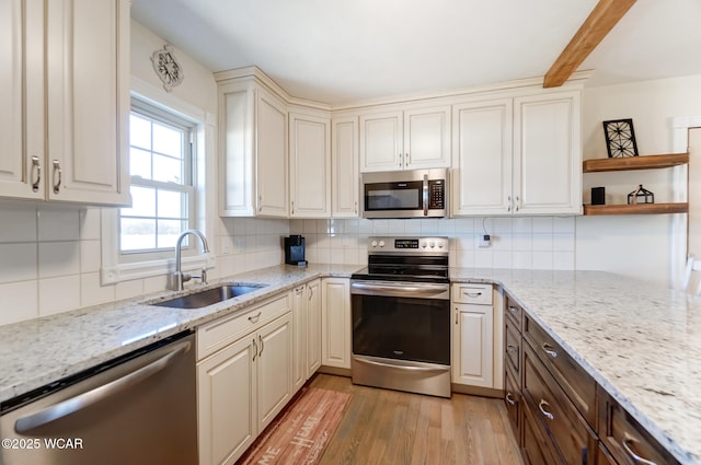 kitchen with sink, light stone counters, tasteful backsplash, light wood-type flooring, and appliances with stainless steel finishes