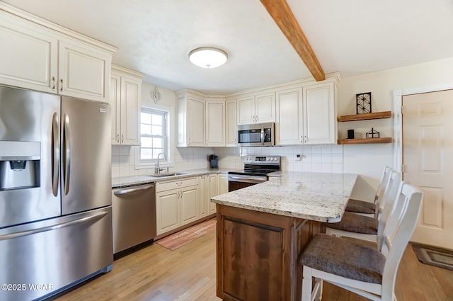 kitchen featuring appliances with stainless steel finishes, backsplash, light stone counters, a kitchen bar, and cream cabinetry