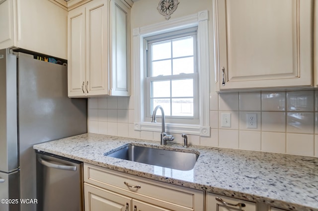 kitchen featuring sink, cream cabinetry, stainless steel appliances, light stone countertops, and backsplash