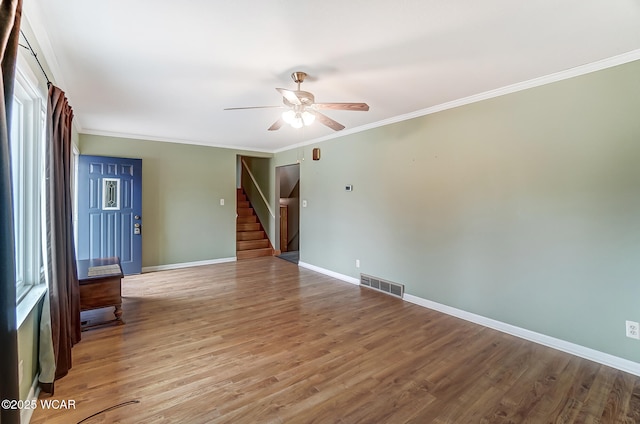 empty room with visible vents, crown molding, baseboards, stairs, and wood finished floors