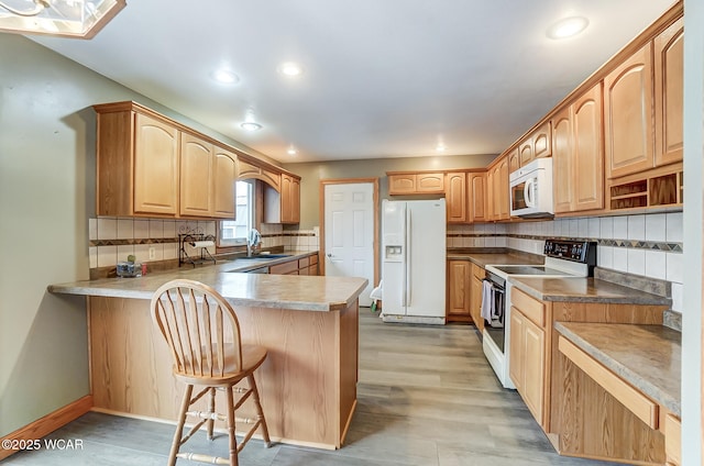 kitchen featuring backsplash, a kitchen bar, a peninsula, white appliances, and a sink