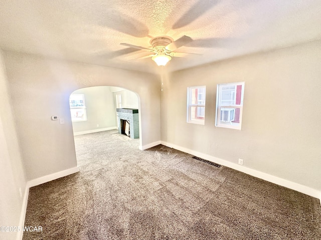 unfurnished living room featuring ceiling fan, carpet floors, a brick fireplace, and a textured ceiling