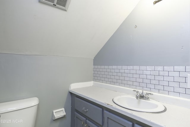 half bath with toilet, visible vents, lofted ceiling, and vanity