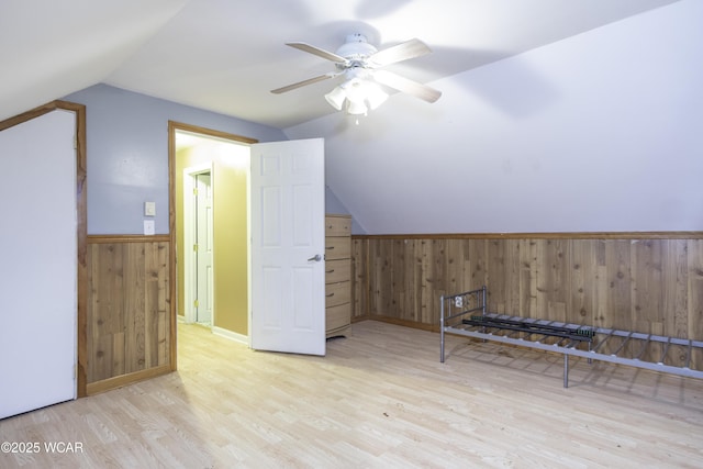 additional living space with light wood-style flooring, wainscoting, vaulted ceiling, wooden walls, and ceiling fan