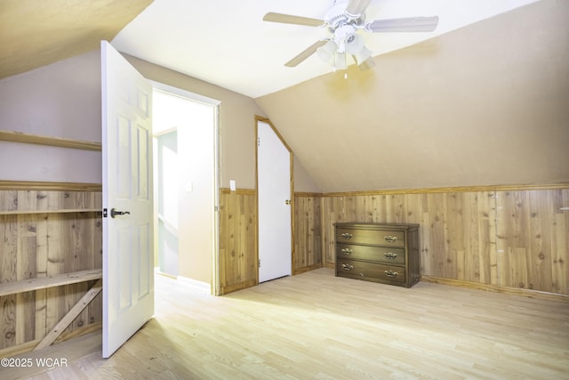 additional living space with a ceiling fan, a wainscoted wall, wood finished floors, vaulted ceiling, and wood walls