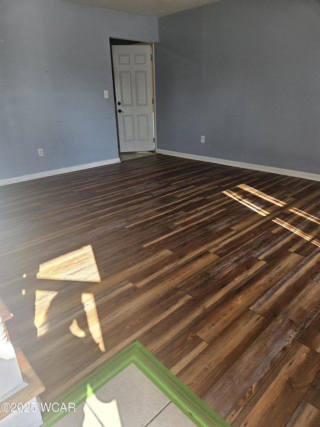 spare room featuring dark wood-style flooring and baseboards