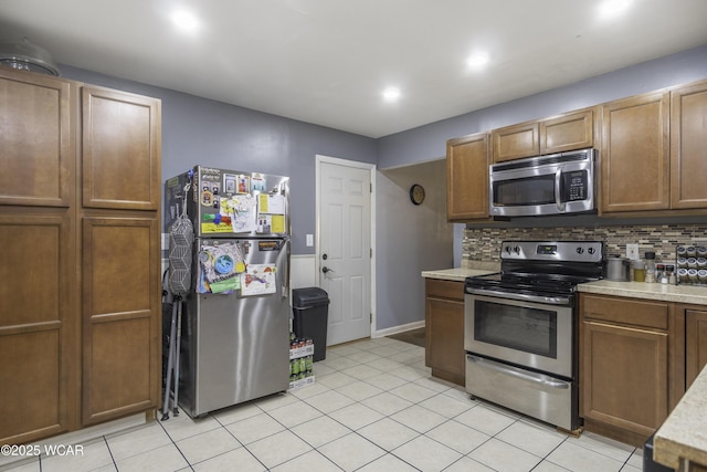 kitchen featuring light tile patterned floors, stainless steel appliances, light countertops, backsplash, and brown cabinets