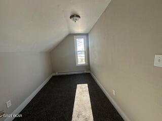 additional living space featuring lofted ceiling, baseboards, dark carpet, and baseboard heating