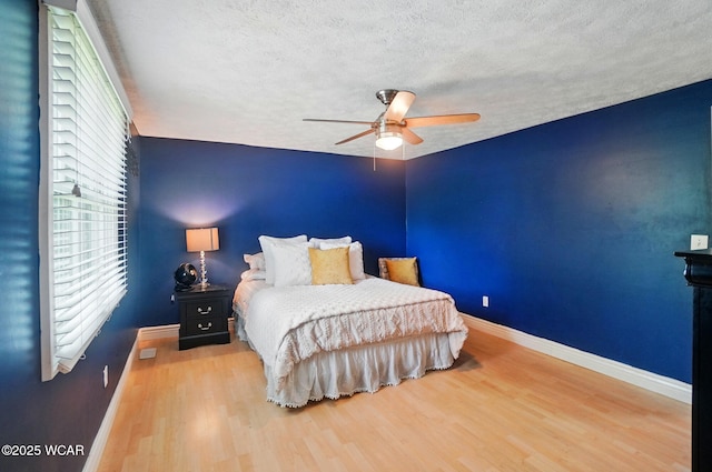 bedroom featuring a ceiling fan, a textured ceiling, wood finished floors, and baseboards