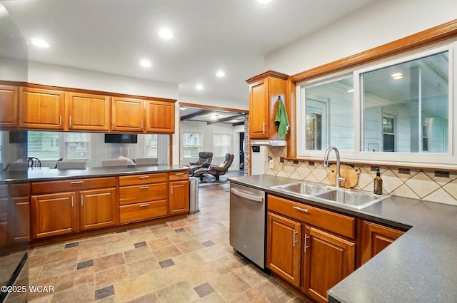 kitchen with brown cabinetry, backsplash, dark countertops, stainless steel dishwasher, and a sink