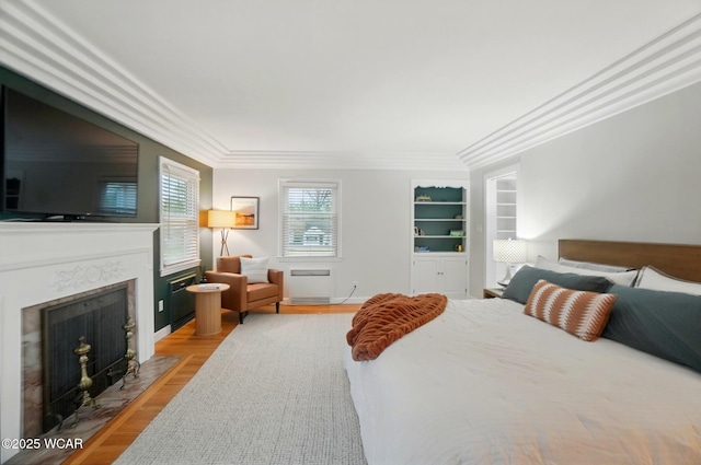 bedroom with crown molding, a fireplace with flush hearth, and wood finished floors