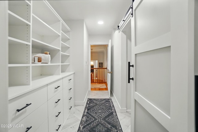 spacious closet featuring a barn door and marble finish floor