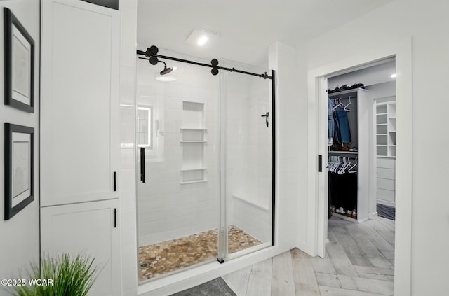bathroom featuring a walk in closet, a stall shower, and wood finished floors