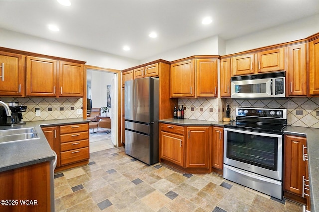kitchen with dark countertops, appliances with stainless steel finishes, a sink, and tasteful backsplash