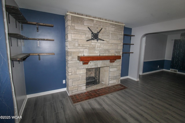 unfurnished living room with dark wood-type flooring and a stone fireplace