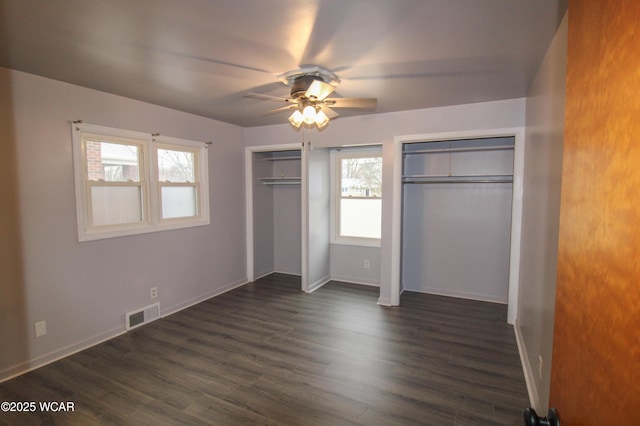 unfurnished bedroom featuring dark hardwood / wood-style floors, two closets, and ceiling fan