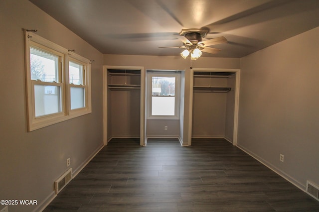 unfurnished bedroom featuring ceiling fan, dark hardwood / wood-style floors, and two closets